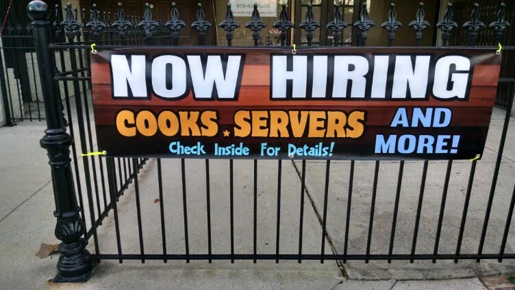 Now Hiring banner on a fence